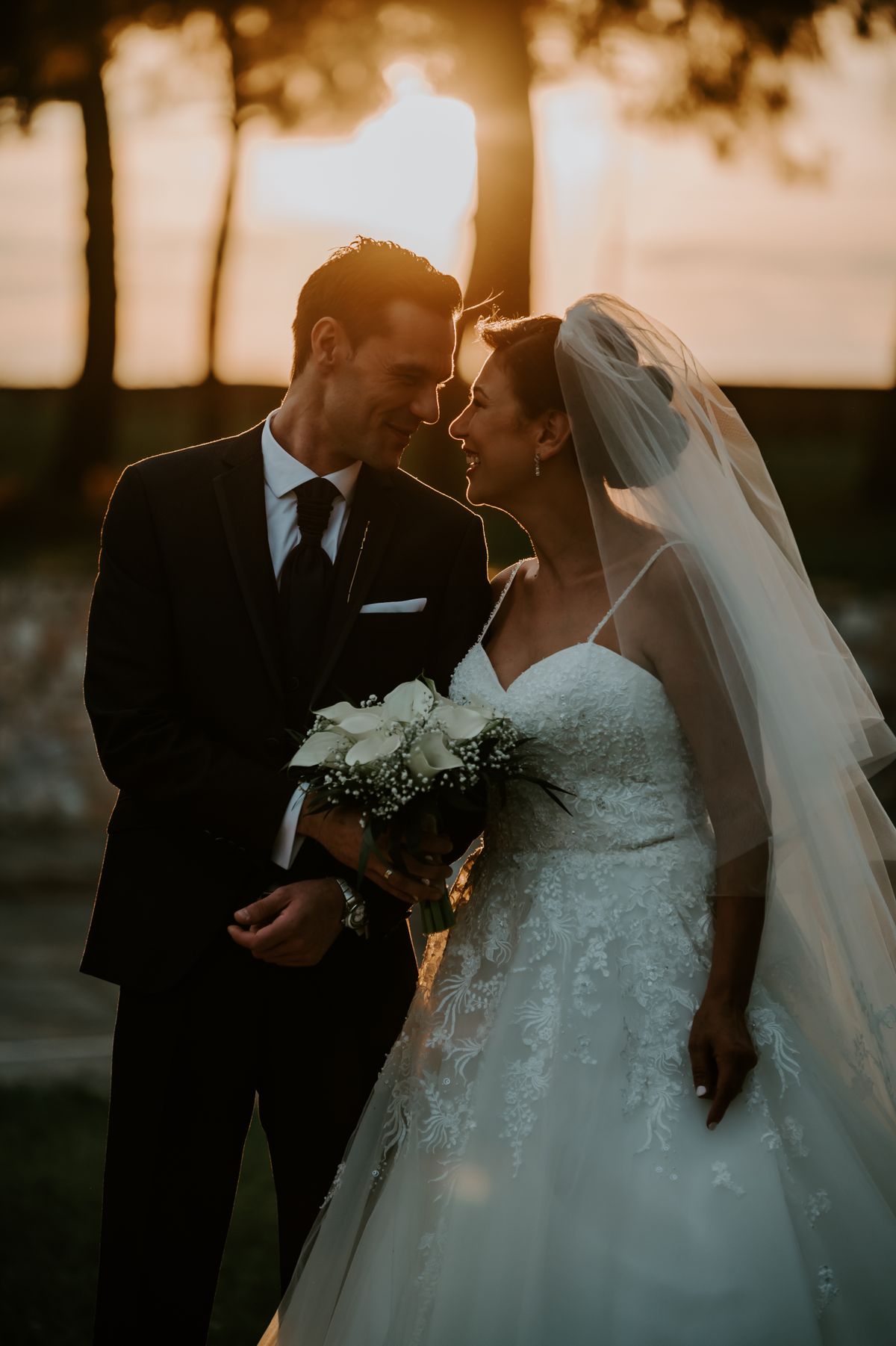 Stock stand-in: a bride and groom nose to nose at golden hour, her veil glowing in the backlight