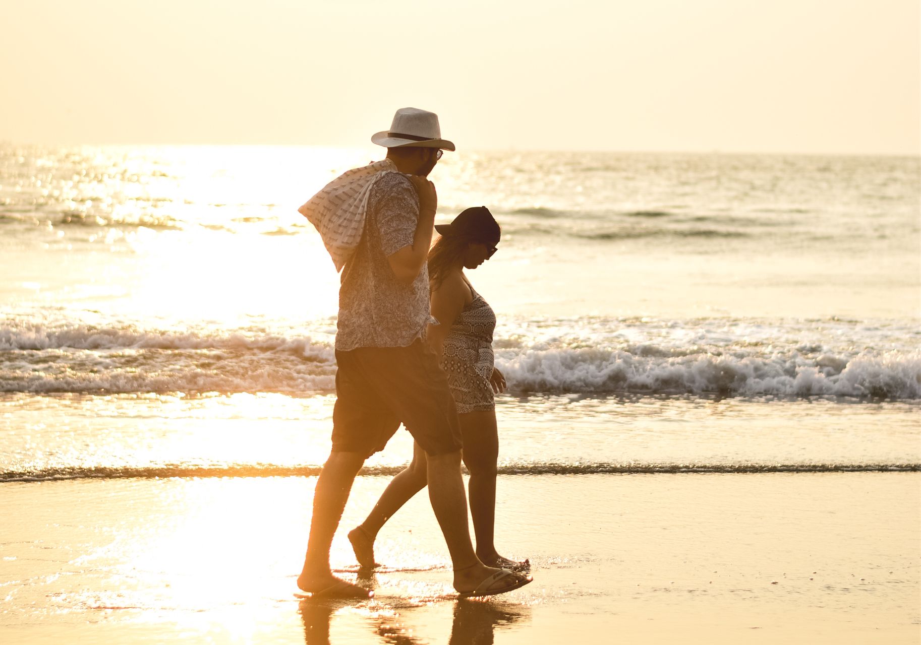 Stock stand-in: a couple walking the surf line, bathed in molten golden sunset light